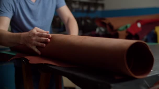 Close-up de mãos artesão desdobramento rolo de couro na mesa dentro de casa — Vídeo de Stock