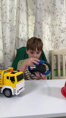 İlkokul çağındaki neşeli genç bir çocuk kapalı bir masada otururken oyuncaklarla oynuyor. Enerji ve hayal gücüyle dolu, rahat, güvenli ve yaratıcı bir ortamda eğleniyor.. 