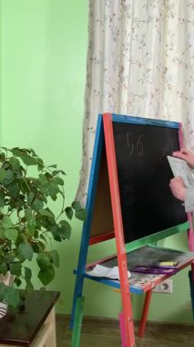 Okul çağındaki çocuk evde ders çalışıyor, ödevlerini özveriyle yapmaya odaklanmış. Öğrenmeyi destekleyen sakin bir ortamda okuma ve sayma, bilgi ve beceriler geliştirme pratiği yapıyor.. 