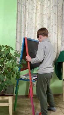 Okul çağındaki çocuk evde ders çalışıyor, ödevlerini özveriyle yapmaya odaklanmış. Öğrenmeyi destekleyen sakin bir ortamda okuma ve sayma, bilgi ve beceriler geliştirme pratiği yapıyor.. 