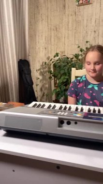 Gözlüklü genç anne evde küçük kızına elektronik piyano ve diğer enstrümanları kullanarak müzik öğretiyor. Birlikte yaratıcı öğrenme, kaynaşma ve müzik becerilerini geliştirmeyi seviyorlar.. 