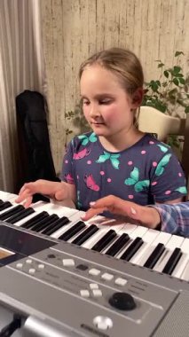 Gözlüklü genç anne evde küçük kızına elektronik piyano ve diğer enstrümanları kullanarak müzik öğretiyor. Birlikte yaratıcı öğrenme, kaynaşma ve müzik becerilerini geliştirmeyi seviyorlar.. 