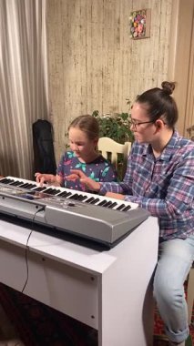 Gözlüklü genç anne evde küçük kızına elektronik piyano ve diğer enstrümanları kullanarak müzik öğretiyor. Birlikte yaratıcı öğrenme, kaynaşma ve müzik becerilerini geliştirmeyi seviyorlar.. 