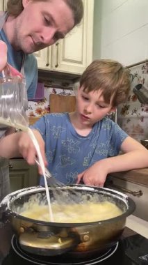 Genç baba ve küçük oğlunun kapalı alanda birlikte yemek pişirdikleri dikey görüntü. Aile tatillerini paylaşırlar, yemek hazırlama ve sıcak bir yuva ortamında eğlenceli etkileşimlerle eğlenirler.. 