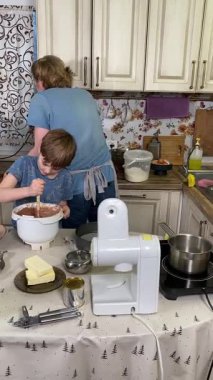 Genç baba ve küçük oğlunun kapalı alanda birlikte yemek pişirdikleri dikey görüntü. Aile tatillerini paylaşırlar, yemek hazırlama ve sıcak bir yuva ortamında eğlenceli etkileşimlerle eğlenirler.. 