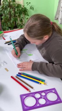 Genç kız evde yaratıcı aktiviteler yapıyor, hobisinin bir parçası olarak kalemlerle resim çiziyor. Odaklanmış ve ilham almış, sanatsal ifadenin günümüze getirdiği eğlence ve rahatlıktan zevk alıyor..