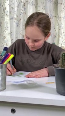 Genç kız evde yaratıcı aktiviteler yapıyor, hobisinin bir parçası olarak kalemlerle resim çiziyor. Odaklanmış ve ilham almış, sanatsal ifadenin günümüze getirdiği eğlence ve rahatlıktan zevk alıyor..