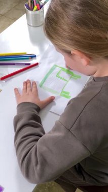 Genç kız evde yaratıcı aktiviteler yapıyor, hobisinin bir parçası olarak kalemlerle resim çiziyor. Odaklanmış ve ilham almış, sanatsal ifadenin günümüze getirdiği eğlence ve rahatlıktan zevk alıyor..
