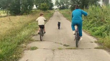 Anne ve oğlu gün batımında yeşil bir çayır boyunca bisiklet sürerken dışarıda mutlu bir aile zamanı. Sıcak akşam güneşi, doğa, rahatlama ve basit kırsal yaşam. Kaygısız ruh hali..