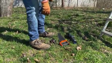 Genç bir adam güneşli bir bahar gününde ağaçları buduyor ve el aletleriyle bahçeyle ilgileniyor. Mevsimlik bahçe işleri, dalları budamak, bahçe bakımı ve parlak güneş ışığında yeni bir başlangıç konsepti.
