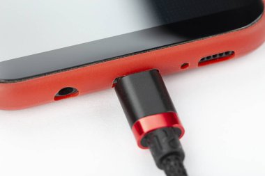 Kırmızı çantalı cep telefonu, beyaz arka planda şarj etmek için bağlı bir kablo. Hücresel iletişim kavramı.