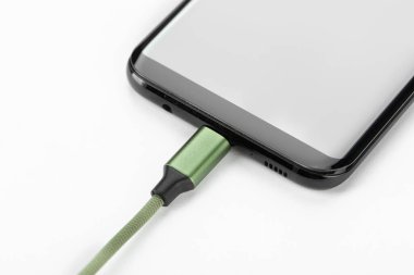 Beyaz arka planda şarj kablosu olan bir cep telefonu. Hücresel iletişim kavramı.