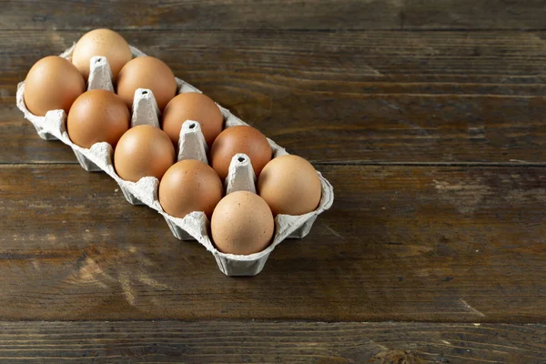 Chicken eggs in an open egg carton on wood background. Top view with copy space. Natural healthy food and organic farming concept.