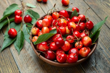 Tahta masadaki kiraz ve kil kasesinde yapraklar..