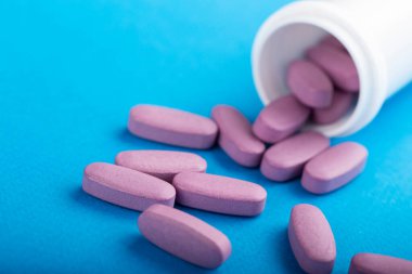 Mavi arka planda beyaz bir şişeden dökülen pembe haplar. Sağlık hizmeti konsepti. Mesaj için yer var. Muhafazakar tıp. Üst görünüm. 