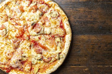 Tahta arka planda pastırmalı, domatesli, mantarlı ve peynirli taze İtalyan pizzası. İtalyan yemeği. Mesaj için yer var. Üst görünüm.