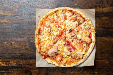 Tahta arka planda pastırmalı, domatesli, mantarlı ve peynirli taze İtalyan pizzası. İtalyan yemeği. Mesaj için yer var. Üst görünüm.