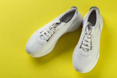 Sarı arka planda bir çift yeni beyaz spor ayakkabı. Rahat rahat ayakkabılar.