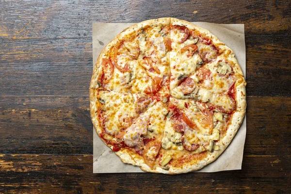 Tahta arka planda pastırmalı, domatesli, mantarlı ve peynirli taze İtalyan pizzası. İtalyan yemeği. Mesaj için yer var. Üst görünüm.