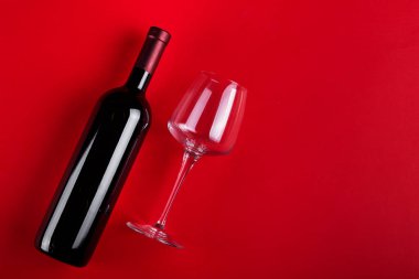 Kırmızı şarap şişesi ve boş şarap kadehi. Kırmızı arka planda. Romantik bir ruh hali. Mesaj için yer var. Üst görünüm.