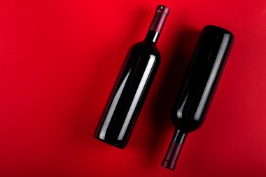 Kırmızı arka planda iki şişe kırmızı şarap. Romantik bir ruh hali. Mesaj için yer var. Üst görünüm.