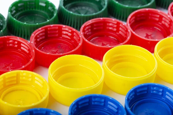 Plastic multi-colored bottle caps are arranged in rows on a white background. Recycling and reuse concept.