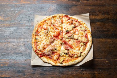 Tahta arka planda pastırmalı, domatesli, mantarlı ve peynirli taze İtalyan pizzası. İtalyan yemeği. Mesaj için yer var. Üst görünüm.