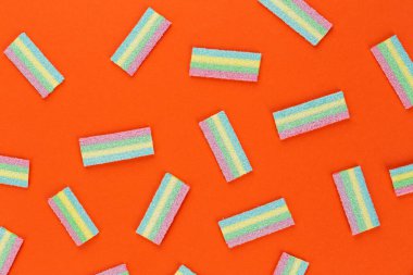 Turuncu arka planda renkli şekerleme deseni. Yumuşak diş etleri yukarıdan görünüyor. Çeşitlilik konsepti. Eşcinsel renkleri. Tatlı yemek tatlısı. Yukarıdan görüntüle