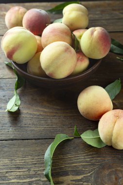 Ahşap bir kırsal masada, kil bir kasede taze şeftali hasadı. Şeftali yaprakları kompozisyonda mevcuttur. Organik meyve, vejetaryen yemeği..