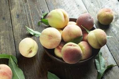 Ahşap bir kırsal masada, kil bir kasede taze şeftali hasadı. Şeftali yaprakları kompozisyonda mevcuttur. Organik meyve, vejetaryen yemeği..