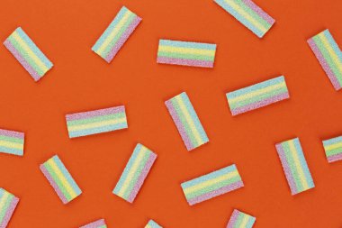 Turuncu arka planda renkli şekerleme deseni. Yumuşak diş etleri yukarıdan görünüyor. Çeşitlilik konsepti. Eşcinsel renkleri. Tatlı yemek tatlısı. Yukarıdan görüntüle