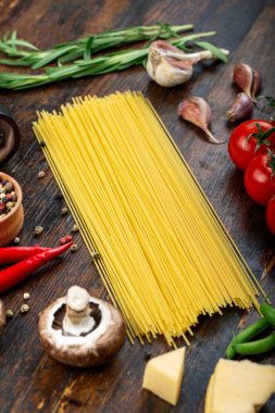 Taze domatesli çiğ makarna, biber, kuşkonmaz fasulyesi, baharat ve peynir ahşap bir masada. İtalyan spagettisi için yemek malzemeleri..
