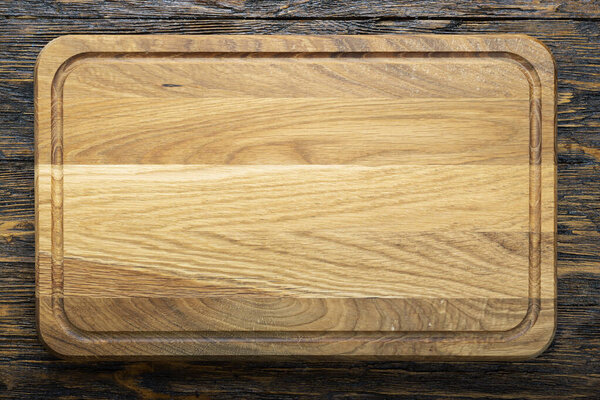 Cutting wooden board of rectangular shape on a wooden background.  Space for text. Top view.