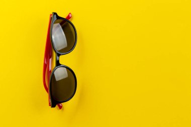 Sarı arka planda kırmızı çerçeveli güneş gözlükleri. Yaz ve tatil konsepti. Mesaj için yer var. Üst görünüm.