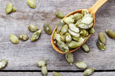 Tahta bir kaşıkta kabak yeşili tohumlar ve ahşap bir masaya serpilmiş. Sağlıklı yiyecekler.