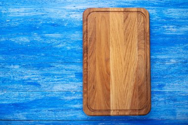 Mavi ahşap bir masada boş dikdörtgen kesme tahtası. Mesaj için yer var. Üst görünüm.