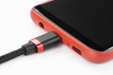 Kırmızı çantalı cep telefonu, beyaz arka planda şarj etmek için bağlı bir kablo. Hücresel iletişim kavramı.
