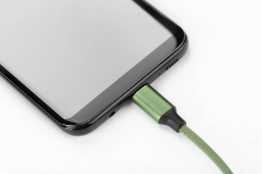 Beyaz arka planda şarj kablosu olan bir cep telefonu. Hücresel iletişim kavramı.
