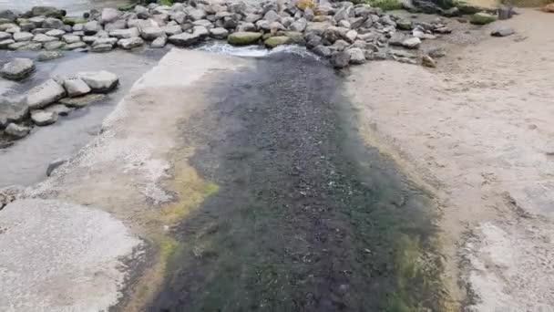 Klar ström av vatten kaskader genom stenarna och rinner ut i havet. — Stockvideo