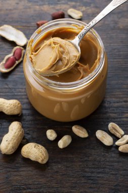 açık kavanozda fıstık ezmesi ve masaya dağılmış kabukta fıstık ezmesi.