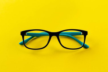 Sarı arka plandaki görüşü düzeltmek için şık gözlükler. Modaya uygun aksesuarlar. Üst görünüm.