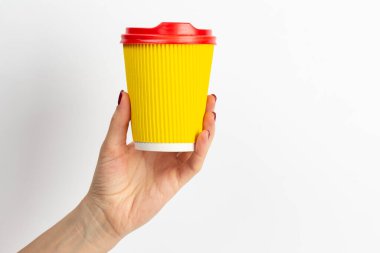 Beyaz arka planda tek kullanımlık kahve fincanı sarısı bir kadın elinde. Yakın plan..