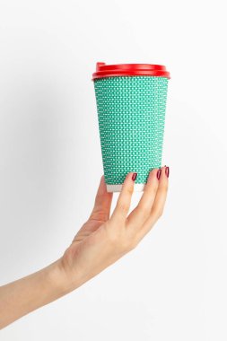 Beyaz arka planda tek kullanımlık kahve fincanı taşıyan kadın eli. Yakın plan..