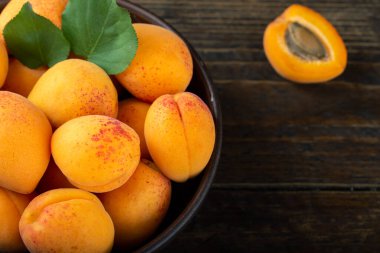 Olgun kayısılar ve kayısı yaprakları ahşap bir masada bir kasede. Ev bahçesinden taze meyve. Sağlıklı yemek..