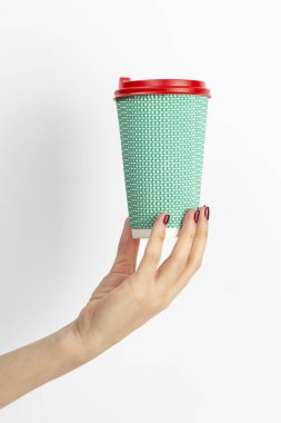 Beyaz arka planda tek kullanımlık kahve fincanı taşıyan kadın eli. Yakın plan..