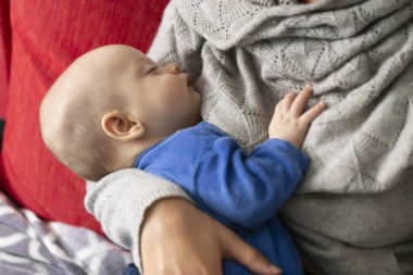 Mavi pijamalı güzel bebek annenin kollarında uyuyor.