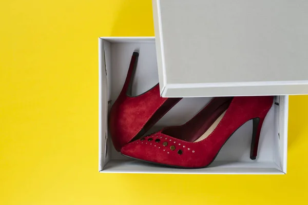 New women\'s red suede shoes in a box on a yellow background. Top view.