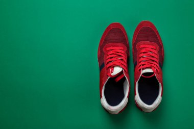 Yeşil arka planda bir çift yeni kırmızı spor ayakkabı. Sıradan ayakkabılar. Mesaj için yer var. Üst görünüm.