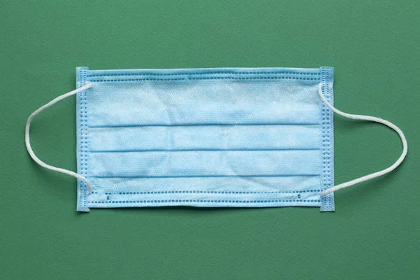 Surgical masks with rubber ear straps on a green background. Typical 3-ply surgical mask to cover the mouth and nose. Procedure mask from bacteria. Top view.