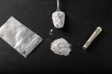 Siyah arka planda plastik pakette kokain, yakın plan. Uyuşturucu kullanımı için sarılmış bir dolar. Yasak uyuşturucular.